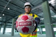A person wearing PPE and holding a soccer ball out in front of themselves.