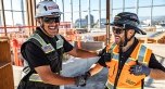 Two people on a jobsite wearing PPE, smiling, and shaking hands