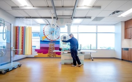 Person in patient bed with another person standing next to the bed