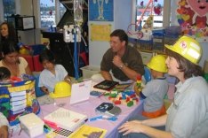 Two adults sitting in a classroom interacting with children.