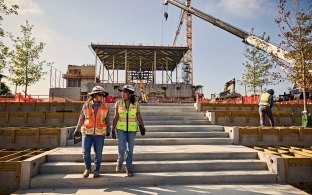 Two people walking down an outdoor staircase on a jobsite. 