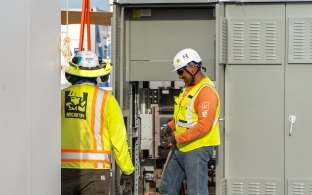 Two people working on an electrical box on a solar project.