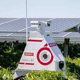 A robot in front of a few rows of solar panels