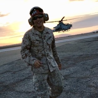 A person wearing a military uniform with a helicopter in the background