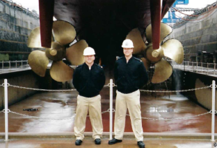 Two people standing in front of ship propellers