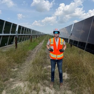 A person wearing PPE standing in a field with solar panels