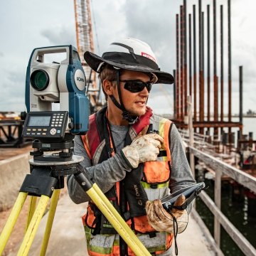 A construction worker operates survey equipment on a busy jobsite.