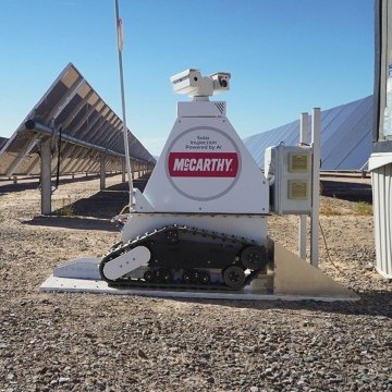 A robot in front of a few rows of solar panels