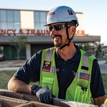 A person with construction PPE standing outside of an emergency and trauma center. 