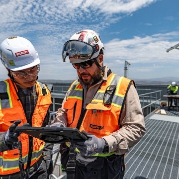 Two people wearing construction PPE at a jobsite while looking at a tablet.