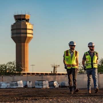 Two people walking with an airport control tower in the background