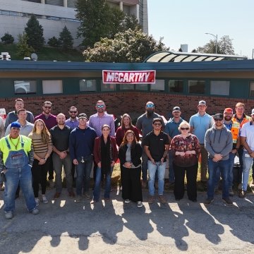 A group of people standing in front of a building with the McCarthy logo hanging in the background.