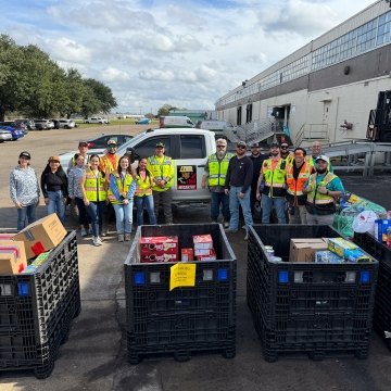 A group of people standing near a few cases of donated food items