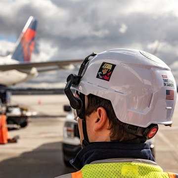 A person wearing PPE in the foreground with an airplane in the background