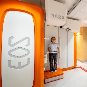 A person standing in the EOS machine while someone else looks on