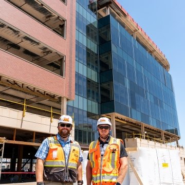 Two people standing in front of a building under construction wearing PPE