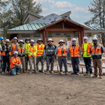 A group of people wearing PPE posing in front of a building under construction.