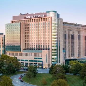 Evening view of the Barnes-Jewish Hospital towers with glass façade reflecting the sunset above treetops