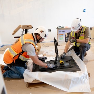Two people wearing PPE and working on a TV