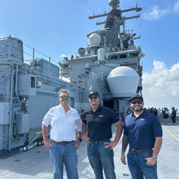 Three people standing in front of a military ship