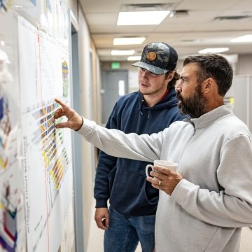 Two people looking at paperwork on the wall. 