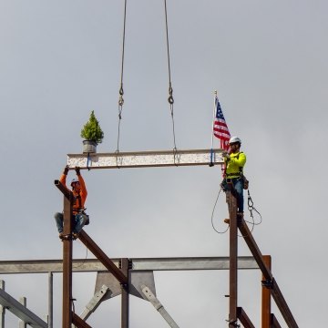 Two people wearing PPE placing the final beam on top of the structure