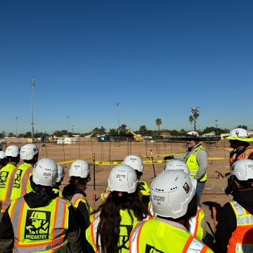 A group of people wearing PPE listening to a person speak
